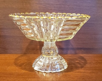 May include: A clear glass pedestal bowl with a gold rim. The bowl has a fluted design and sits on a pedestal base.