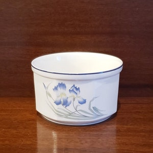 May include: White ceramic planter with a blue and green floral design. The planter has a rounded bottom and a straight rim.