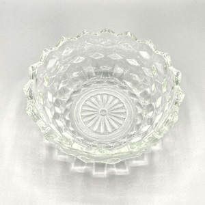 May include: A clear glass bowl with a diamond pattern and a scalloped edge. The bowl is empty and has a reflective surface.