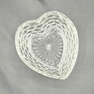 Puede incluir: Plato transparente en forma de corazón de cristal con un diseño geométrico texturizado. El plato tiene una apariencia en capas, con una forma de corazón central que presenta un patrón de rayos de sol. Los bordes exteriores tienen un patrón de diamantes.