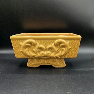 Maceta de cerámica vintage rectangular marrón miel con patas, textura y un gran lazo elaborado.