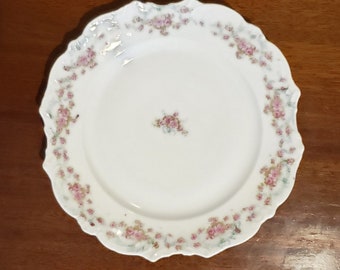 May include: A white porcelain plate with a scalloped edge and a delicate floral pattern in shades of pink and green.