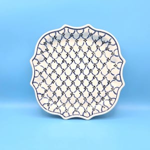 Könnte beinhalten: Eine weiße Keramik-Servierplatte mit einem blauen und weißen geometrischen Muster. Die Platte hat einen gewellten Rand.