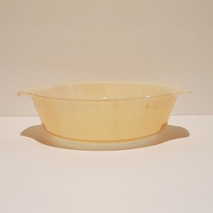 Puede incluir: Un plato para hornear de cerámica de color amarillo pálido con dos asas. El plato es ligeramente translúcido y tiene un borde blanco.