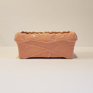 Può includere: Un vaso da fiori rettangolare in ceramica rosa pallido con un motivo decorativo a foglie.