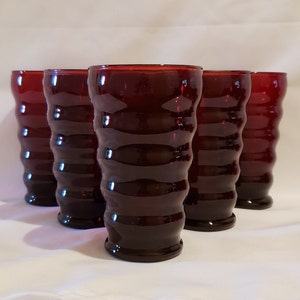 May include: Set of five ruby red glass tumblers with a wavy design. The glasses are clear and have a smooth, rounded bottom.