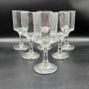 Puede incluir: Seis copas de vino transparentes con cuencos cuadrados y bases con tallo. Las copas están dispuestas en semicírculo, mostrando su textura única y burbujeante. Ideales para servir bebidas.
