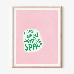 Op de afbeelding: Een roze ingelijste print met de tekst "I just need some space" in groene letters op een witte achtergrond.