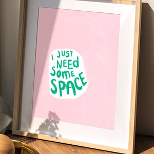Op de afbeelding: Een ingelijst print met een roze achtergrond en witte tekst die "Ik heb gewoon wat ruimte nodig" in groene letters zegt.