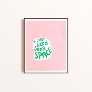 Op de afbeelding: Een ingelijst print met een roze achtergrond en een witte wolk met de tekst "I just need some space" in groene letters.