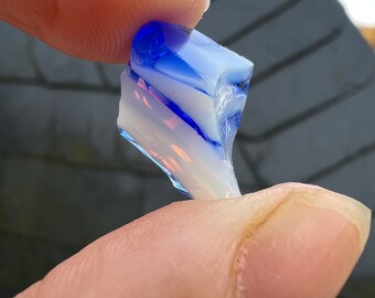 May include: A piece of blue and white dichroic glass with a swirl pattern. The glass is translucent and has a slight iridescent sheen.