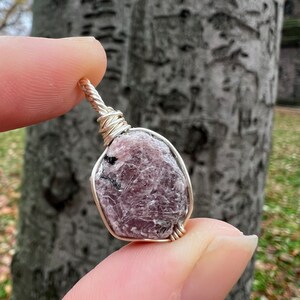 May include: A pink and grey gemstone wrapped in silver wire, creating a pendant.