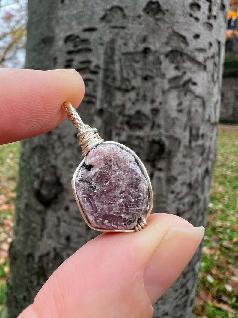 May include: A pink and grey gemstone wrapped in silver wire, creating a pendant.