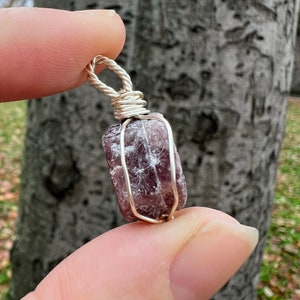 May include: A purple and silver wire-wrapped crystal pendant. The crystal is a natural, rough-cut stone with a deep purple hue. The wire wrapping is silver and adds a delicate touch to the pendant.