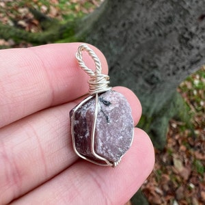 May include: A pink ruby gemstone wrapped in silver wire, forming a pendant.