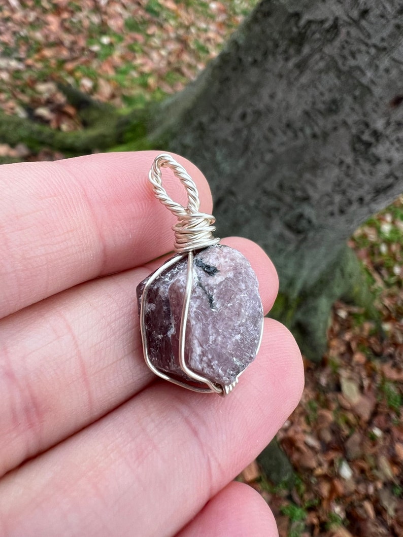 May include: A pink ruby gemstone wrapped in silver wire, forming a pendant.