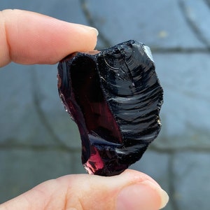 Könnte beinhalten: Ein dunkelvioletter und schwarzer Obsidian-Stein mit einer glatten, glasartigen Oberfläche.