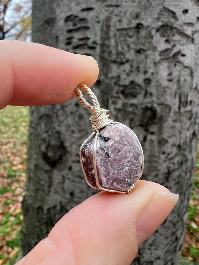 May include: A pink and purple gemstone pendant wrapped in silver wire. The gemstone has a rough, natural texture.