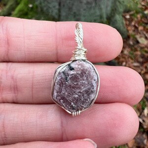 May include: A silver wire-wrapped pendant featuring a raw, light purple and gray gemstone. The gemstone has a rough, natural texture.