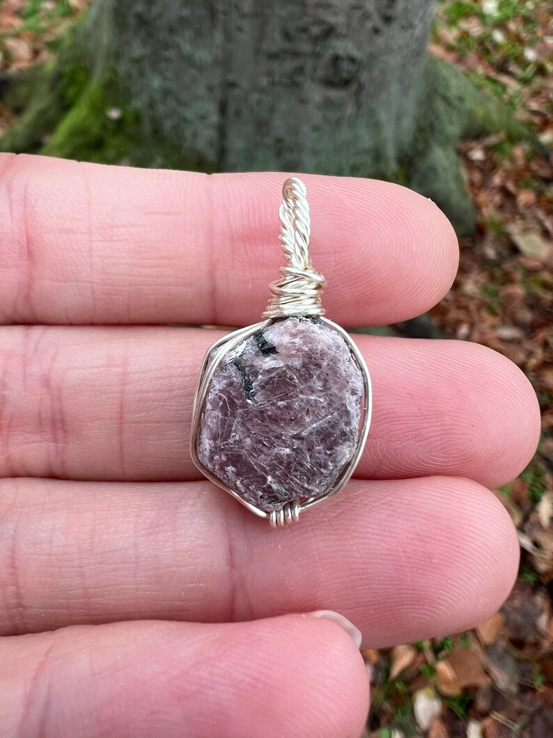 May include: A silver wire-wrapped pendant featuring a raw, light purple and gray gemstone. The gemstone has a rough, natural texture.