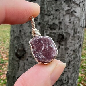 May include: A purple and gray gemstone wrapped in silver wire, creating a pendant.