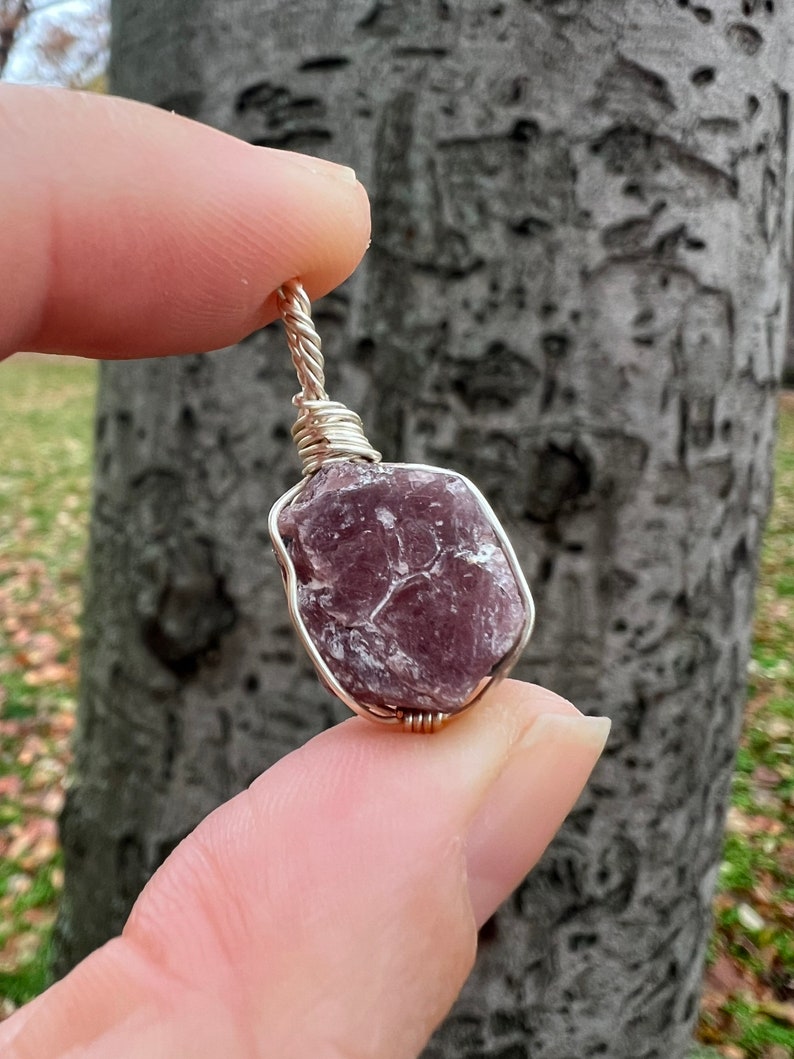 May include: A purple and gray gemstone wrapped in silver wire, creating a pendant.