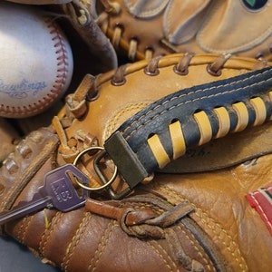 May include: A brown leather baseball mitt with a black and yellow leather strap. A silver key is attached to the strap. The mitt has a red and white label with the word "Wings" on it.