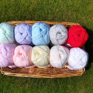 May include: A wicker basket filled with balls of yarn in various pastel colors, including light blue, pink, yellow, and white, along with a single red ball of yarn.