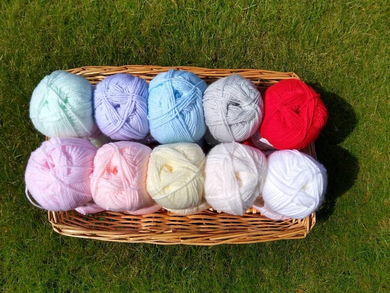 May include: A wicker basket filled with balls of yarn in various pastel colors, including light blue, pink, yellow, and white, along with a single red ball of yarn.