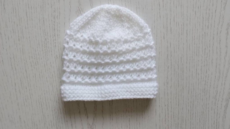 May include: A white crocheted baby hat with a delicate stitch pattern.