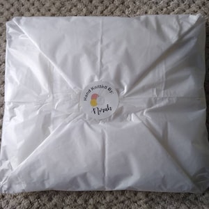 May include: White tissue paper packaging with a round sticker that says "Hand Knitted By: Norah" with a colorful yarn ball and knitting needles graphic.