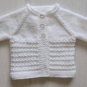 May include: White knitted baby cardigan with a button closure. The cardigan has a textured pattern and is made of soft yarn.