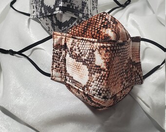 Puede incluir: Dos mascarillas de tela con estampado de piel de serpiente. Una mascarilla es negra y blanca, la otra es marrón y blanca.