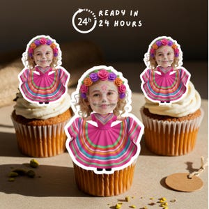 May include: Three cupcakes with white icing, each decorated with a sticker of a girl in a Day of the Dead costume. The stickers show a girl wearing a pink dress and a floral crown. The text "READY IN 24 HOURS" is in the top left.
