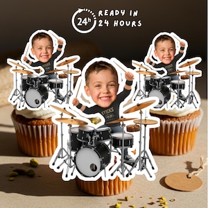 Könnte beinhalten: Drei Cupcakes, verziert mit essbaren Bildern eines Jungen, der Schlagzeug spielt. Der Junge trägt ein schwarzes T-Shirt mit dem Wort "STICKS". Die Cupcakes haben weißes Frosting und essbare Bilddekorationen. Der Text "READY IN 24 HOURS" ist im Hintergrund.