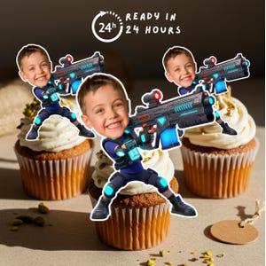 Może przedstawiać: Babeczki z białym lukrem i kreskówkowymi obrazkami chłopca trzymającego futurystyczny pistolet laserowy. Obraz zawiera tekst "READY IN 24 HOURS". Babeczki są udekorowane złotymi posypkami i pistacjami.
