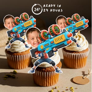 May include: Cupcakes topped with white frosting and a cartoon image of a boy holding a blue and orange toy gun. The image includes the text "READY IN 24 HOURS".