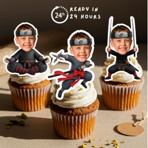 Puede incluir: Tres cupcakes cubiertos con glaseado blanco y adornos con temática ninja. Los adornos presentan la cara de un niño en varias poses de ninja, sosteniendo armas. La imagen incluye el texto "READY IN 24 HOURS".
