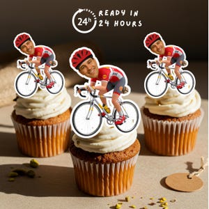 May include: Three cupcakes topped with white frosting and cyclist toppers. The cyclist toppers feature a smiling man in a red and gray cycling outfit riding a yellow and silver bicycle. The text "READY IN 24 HOURS" is in a circle above the cupcakes.