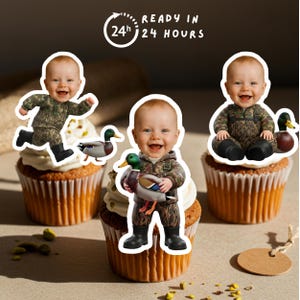 Puede incluir: Tres cupcakes con figuras de beb&eacute;s sonrientes con trajes de camuflaje, cada uno con una figura de pato. Los cupcakes tienen glaseado blanco y est&aacute;n sobre una superficie marr&oacute;n claro. El texto dice "READY IN 24 HOURS".