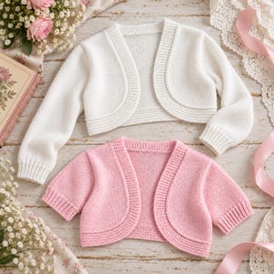 May include: A white long-sleeve knit bolero cardigan and a pink short-sleeve knit bolero cardigan. Both garments feature a rounded open front, ribbed cuffs, and a textured knit border along the edges, showcasing a simple and clean design.