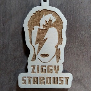Może przedstawiać: Drewniana ozdoba choinkowa przedstawiająca sylwetkę Davida Bowie jako Ziggy Stardust z napisem "Ziggy Stardust" poniżej.