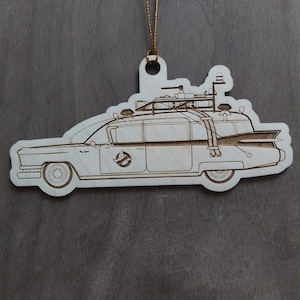 May include: A wooden ornament shaped like the Ghostbusters car, the Ecto-1, with a gold string for hanging.