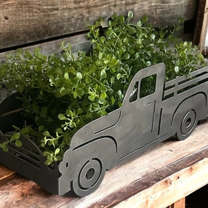May include: A black metal planter shaped like a vintage pickup truck with a bed full of green plants.