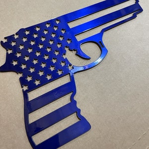 May include: A blue metal cutout of a handgun in the shape of the American flag. The stars and stripes are cut out of the metal, creating a unique and patriotic design.