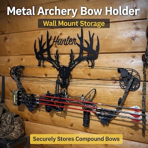 May include: A black metal archery bow holder mounted on a wooden wall, featuring a deer antler design with the word "Hunter". The holder securely stores compound bows and has the text "Wall Mount Storage" and "Securely Stores Compound Bows".