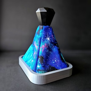 May include: A galaxy-themed gear shift knob with a black diamond-shaped top. The knob is made of fabric and has a grey base.