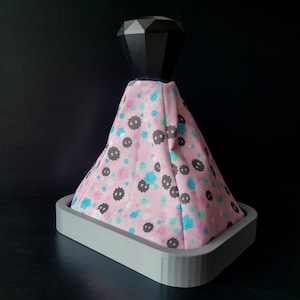 May include: A pink and blue patterned gear shift knob with a black diamond-shaped top. The knob is on a grey base.