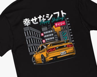May include: A black t-shirt with a yellow car illustration and Japanese text that reads "Happy Shifting!" in English. The car is driving through a city with tall buildings in the background.