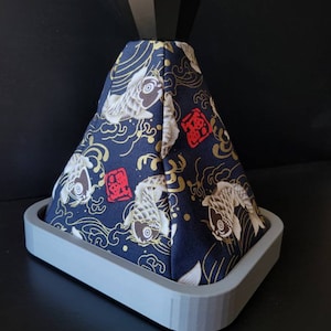 May include: A black and gold patterned gear shift knob with a black diamond-shaped top. The knob is on a grey base.